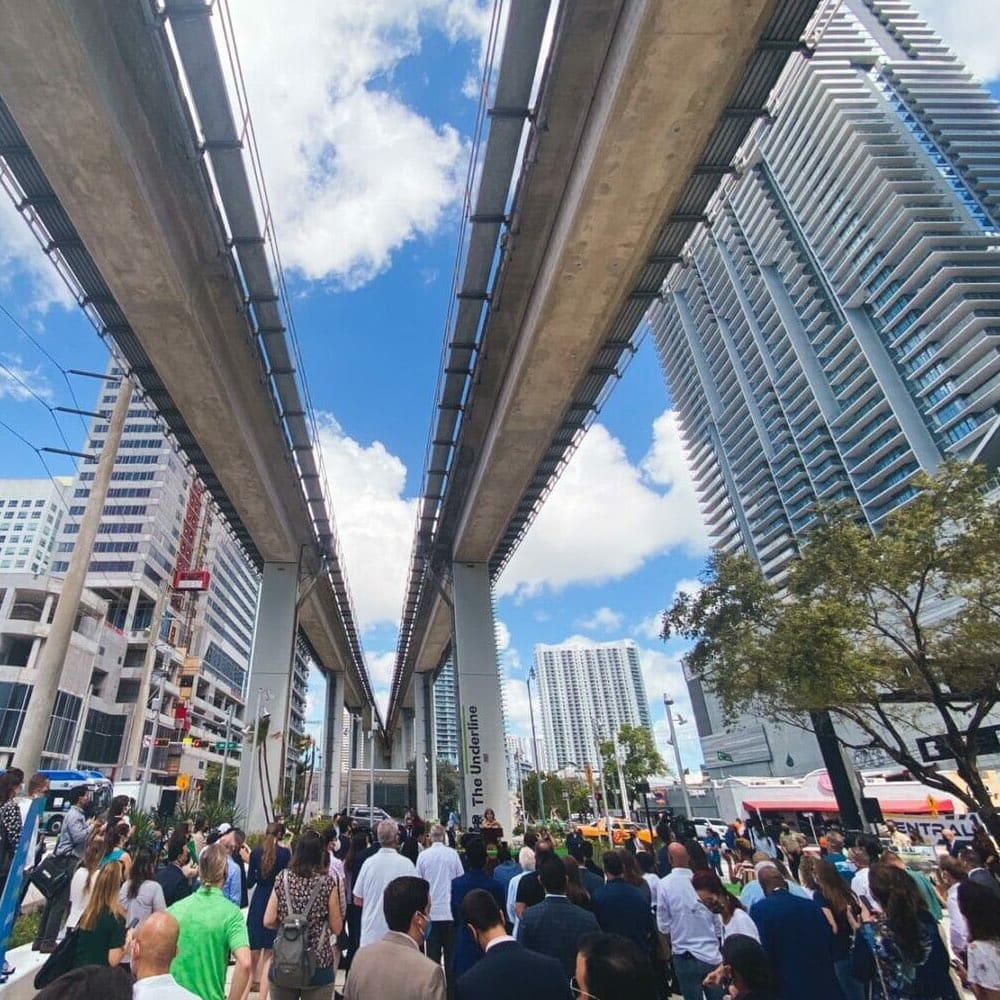 Pedestrians walking under a railway overpass in a busy, modern city
